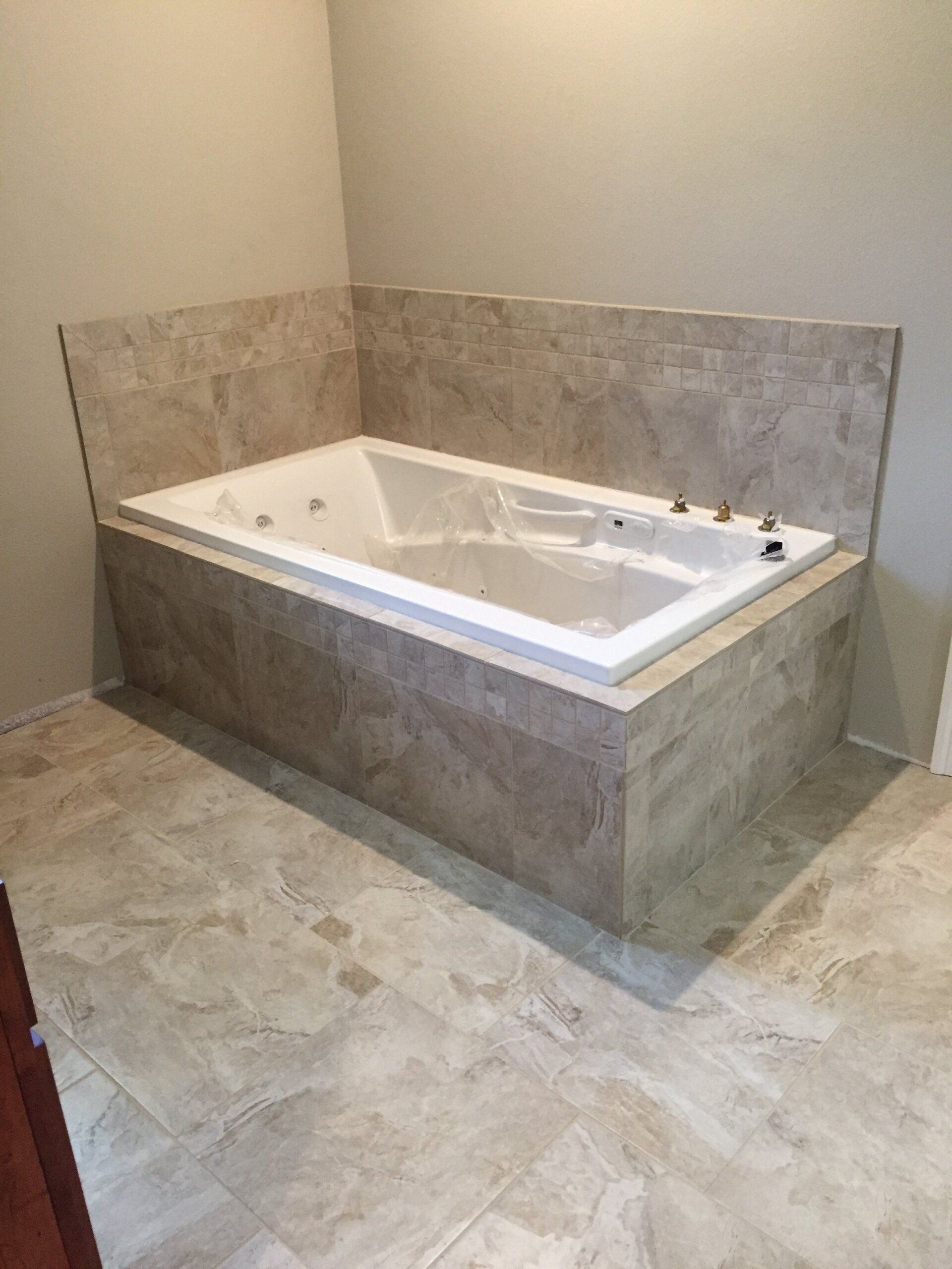 A tile-surrounded white jacuzzi tub in a bathroom with neutral-toned flooring and walls.