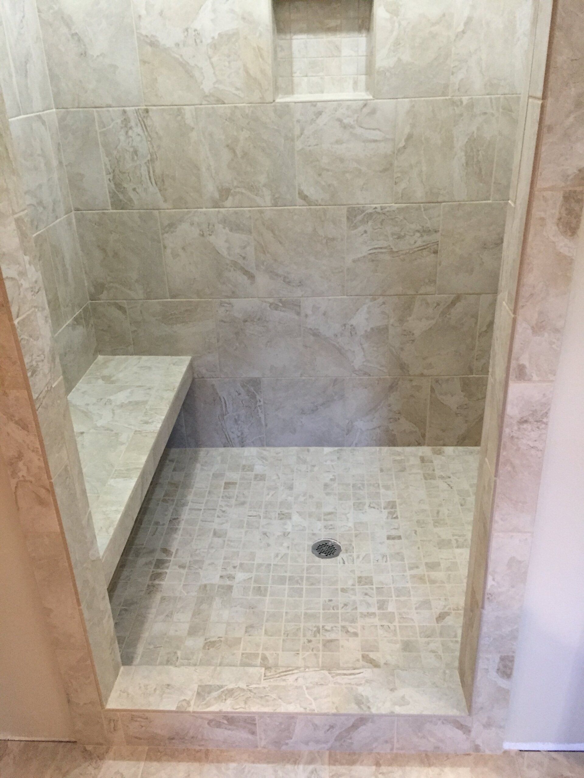 Tile shower with built-in bench and recessed niche. Beige stone tiles on walls and floor.
