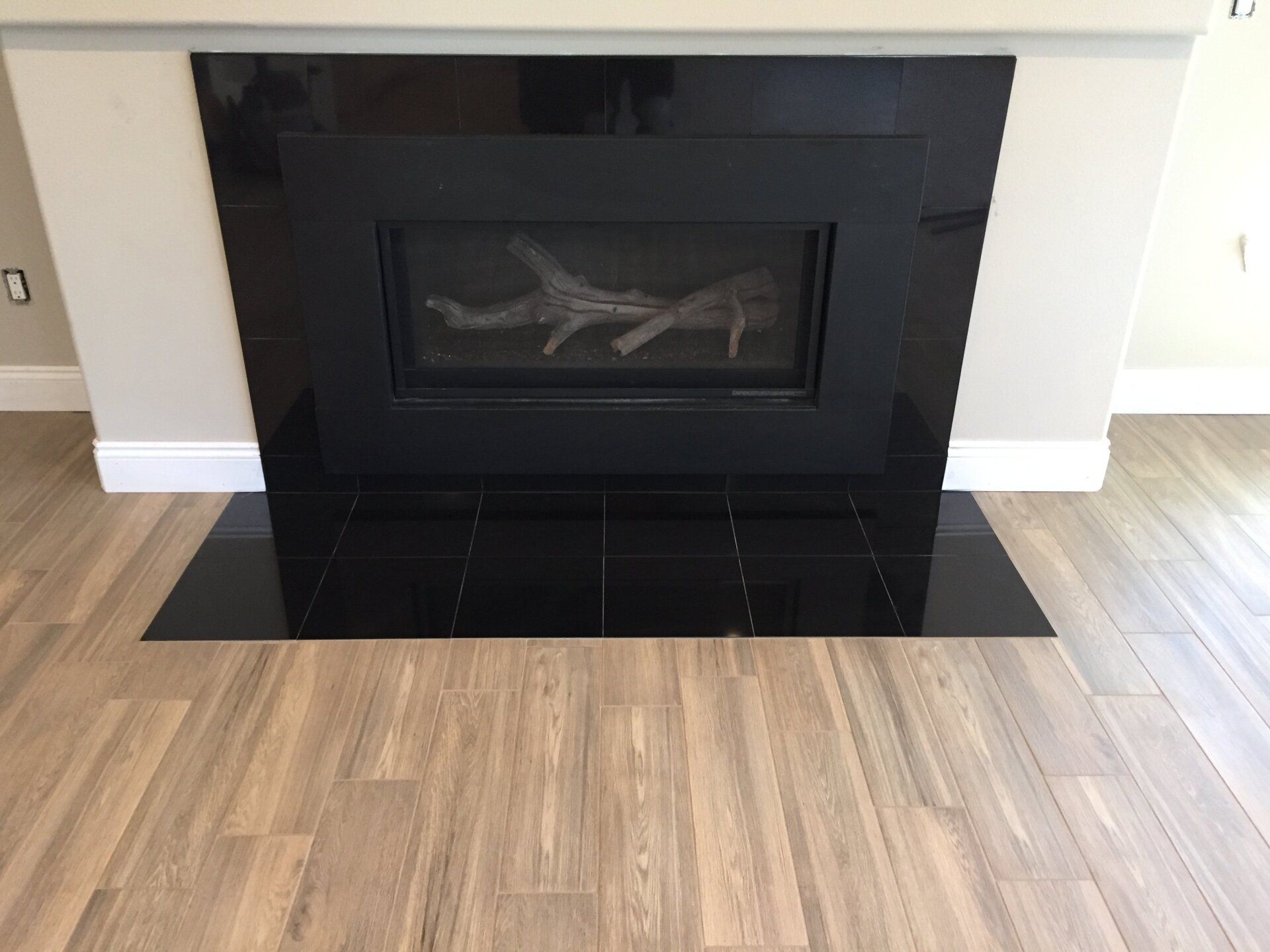 Black tiled fireplace with a gas insert, set against tan walls and wood-look flooring.