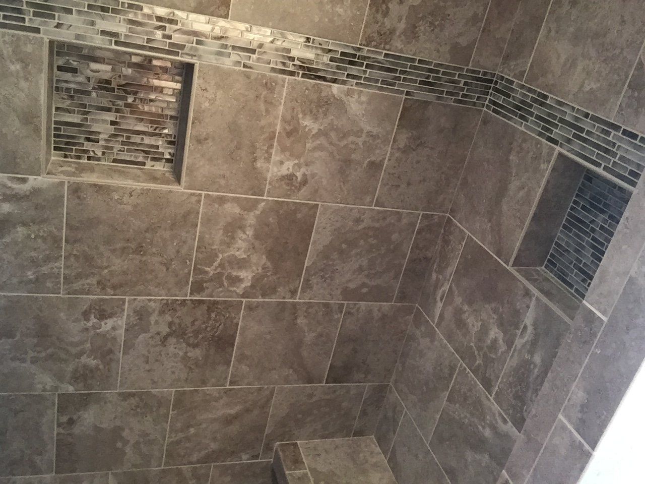 Bathroom shower with brown tile walls and decorative mosaic accents. Two built-in shelf niches.