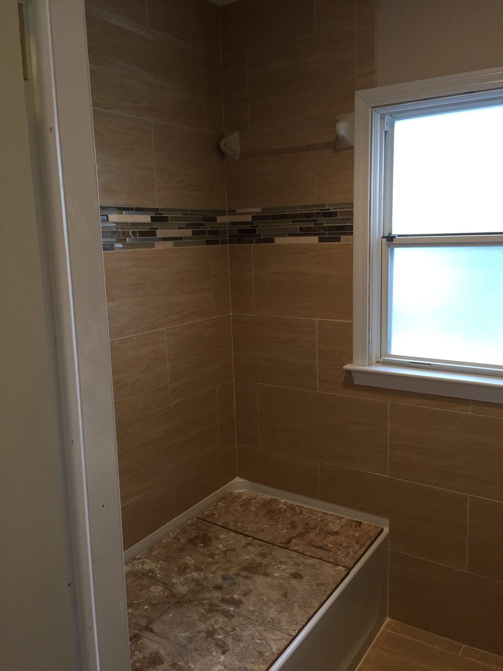 Bathroom with beige tile, a small window, and a built-in bench. Decorative tile strip near the top.