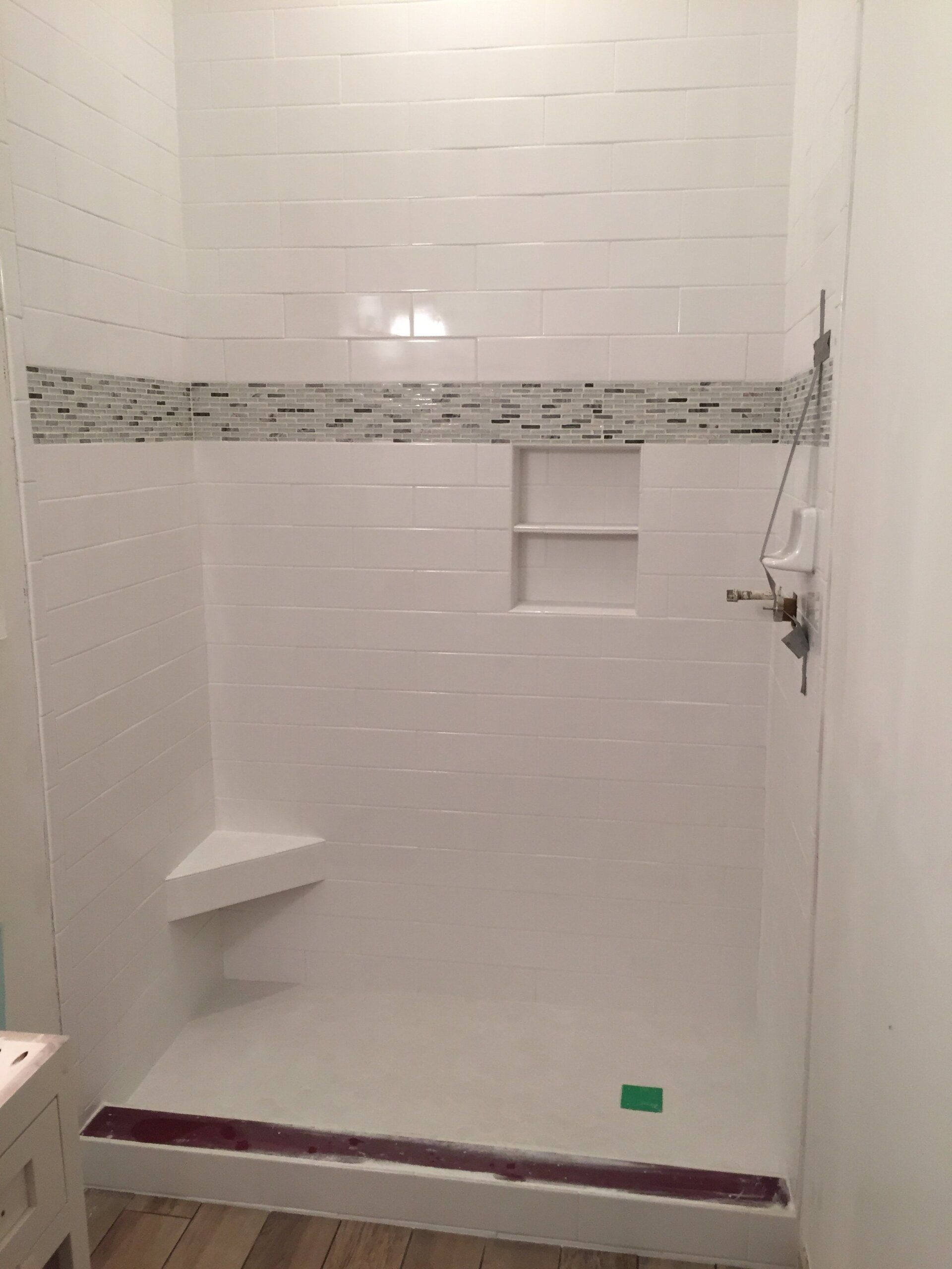 White tiled shower with a mosaic band and built-in corner seat and shelf.