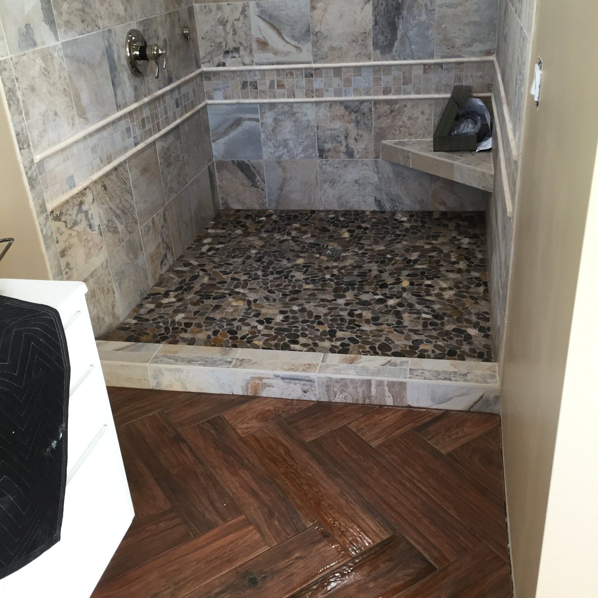 Shower with stone tile walls, pebble floor, and wood-look herringbone tile floor.