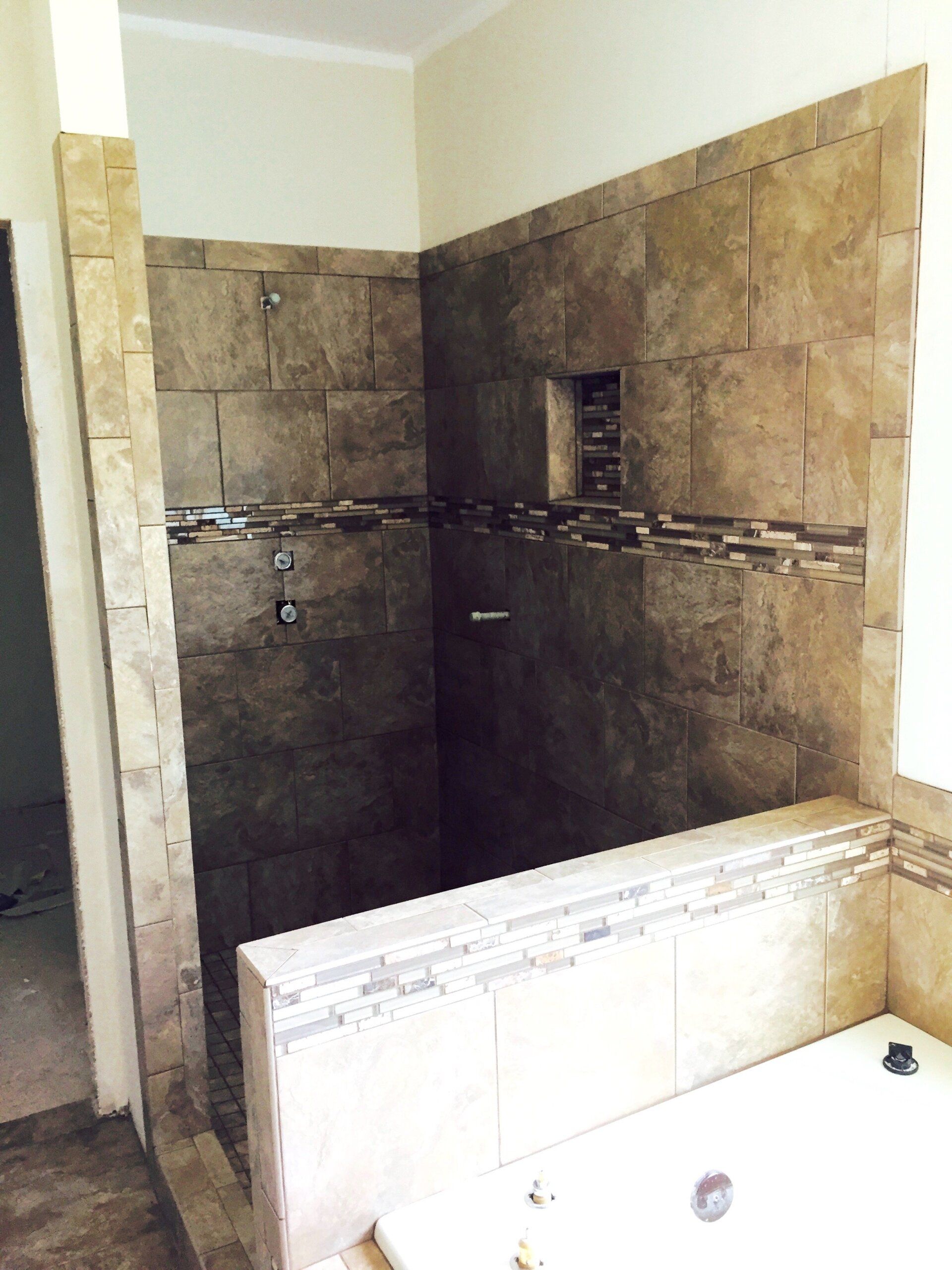 Bathroom shower with tan tile walls, accented with a decorative mosaic strip and a recessed shelf.
