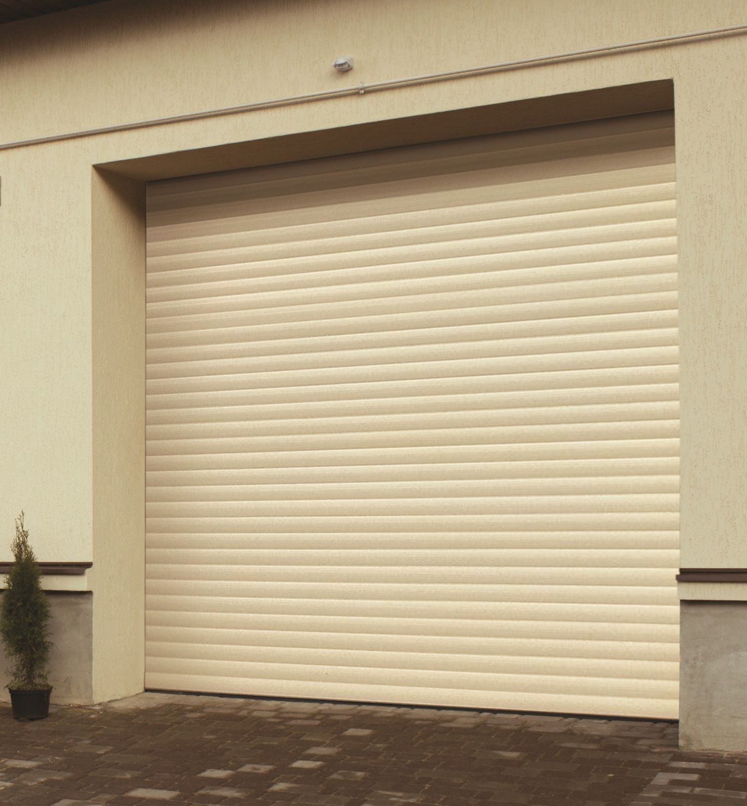A closed beige roller shutter garage door installed on a building exterior with a paved driveway.