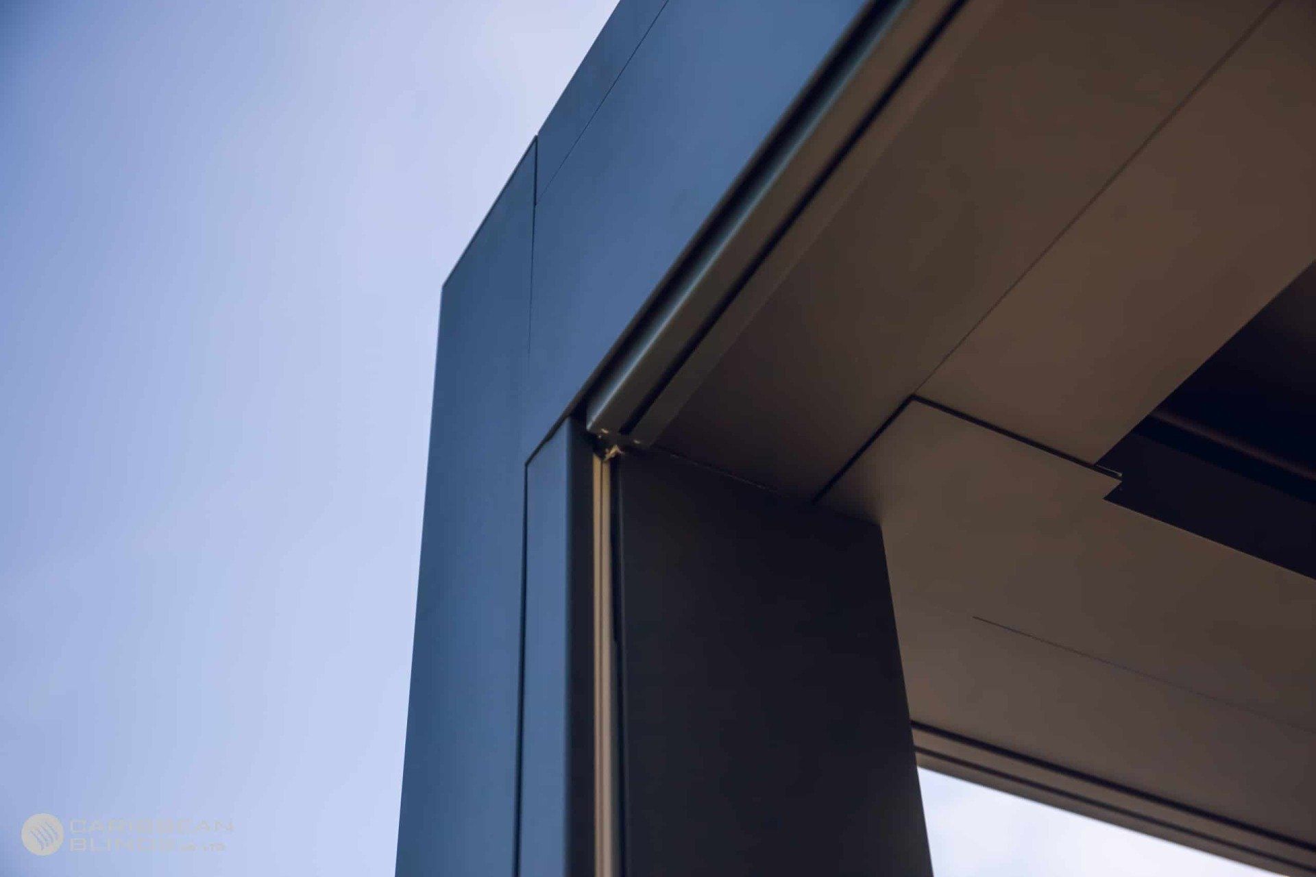 A close-up of a modern building's architectural corner featuring gray metal paneling against a clear blue sky.