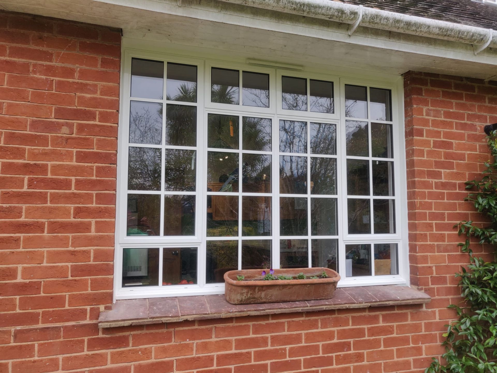 A white-framed window with small panes set in a red brick wall, with a rectangular planter on the stone sill.