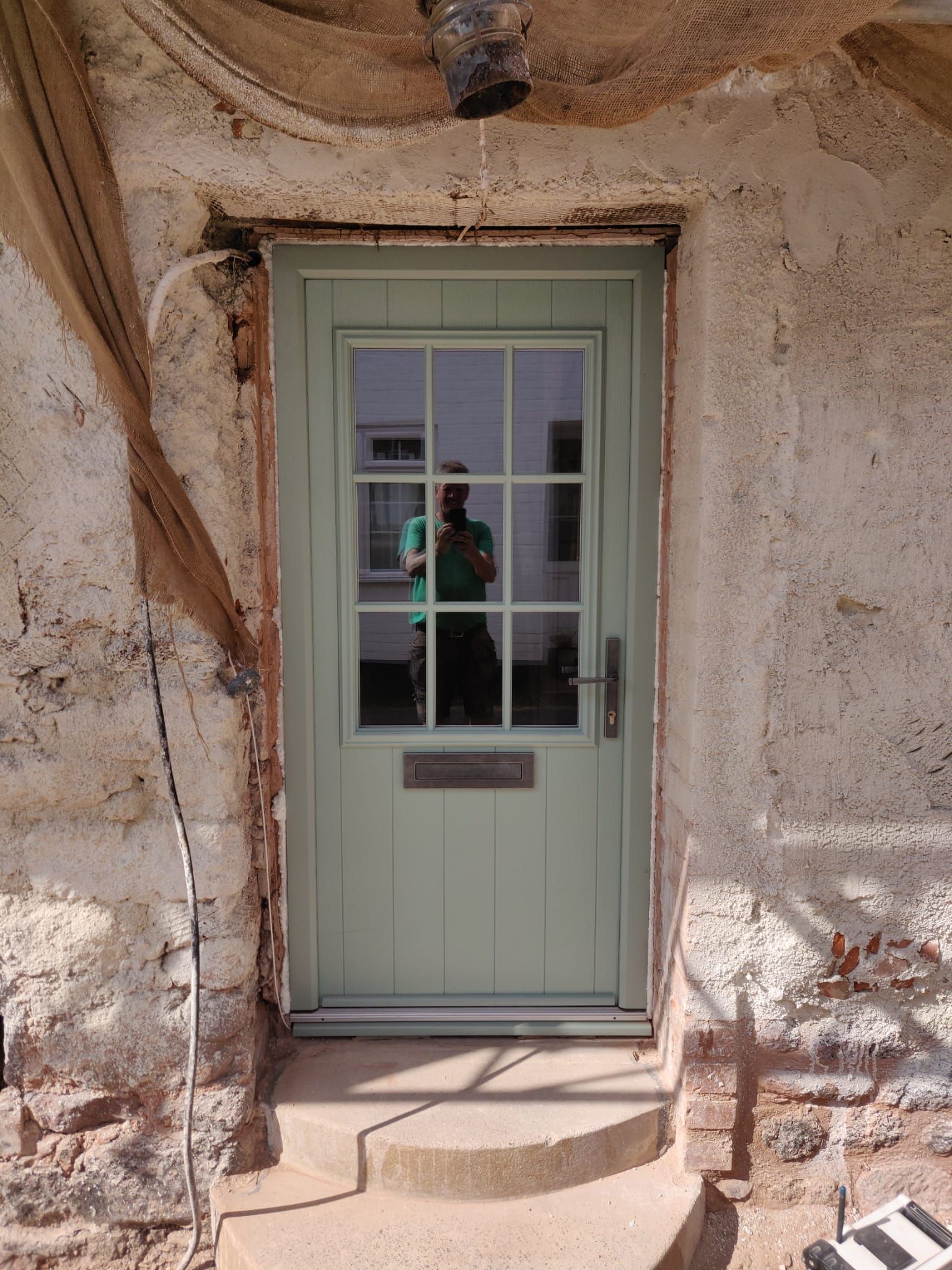 A sage green door with a six-pane glass window is set into a rustic, unfinished stone wall with a small concrete step.