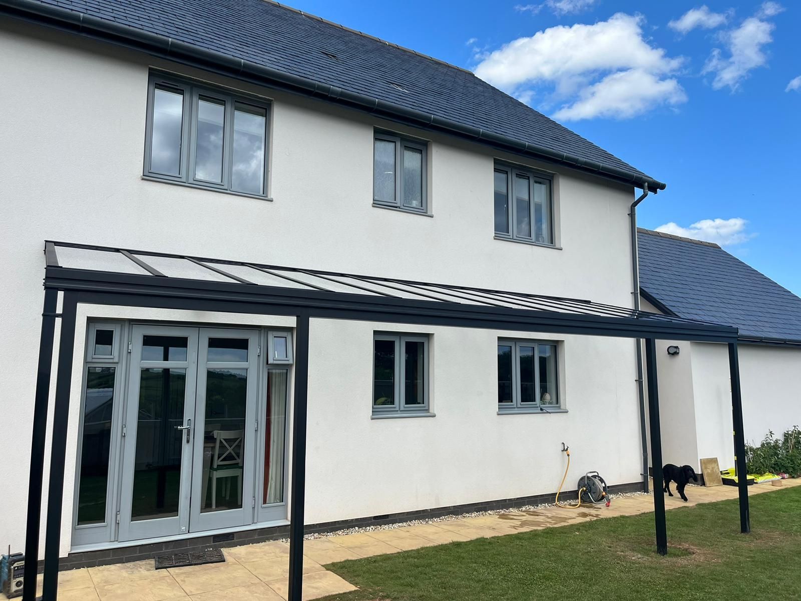A white two-story house with grey window frames and a black patio canopy extending over glass French doors on a sunny day.