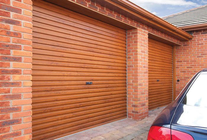 A brick garage exterior with two wooden-style, horizontal-slatted garage doors and the side of a car parked in front.