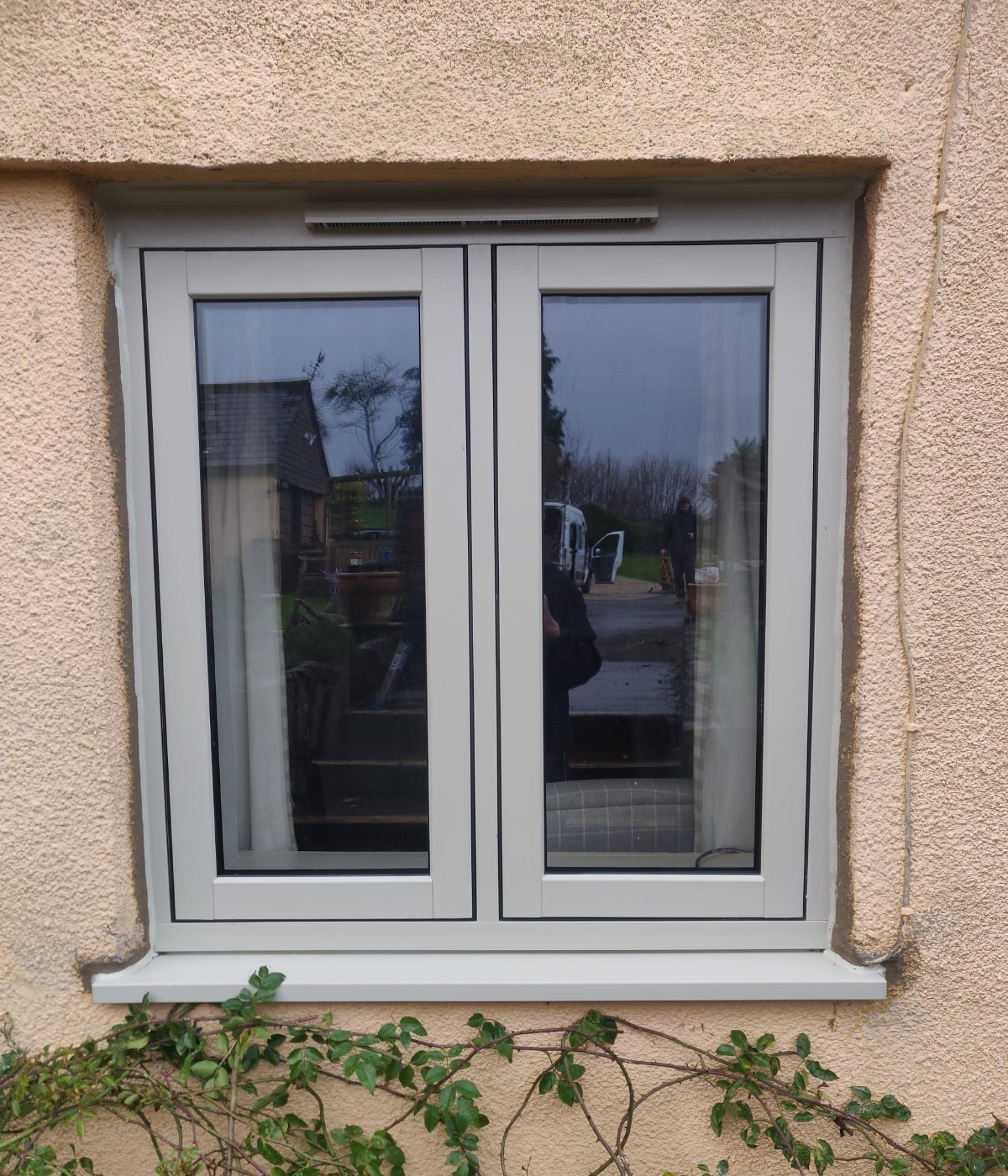 A light gray, dual-pane window frame set into a textured, tan-colored exterior wall.