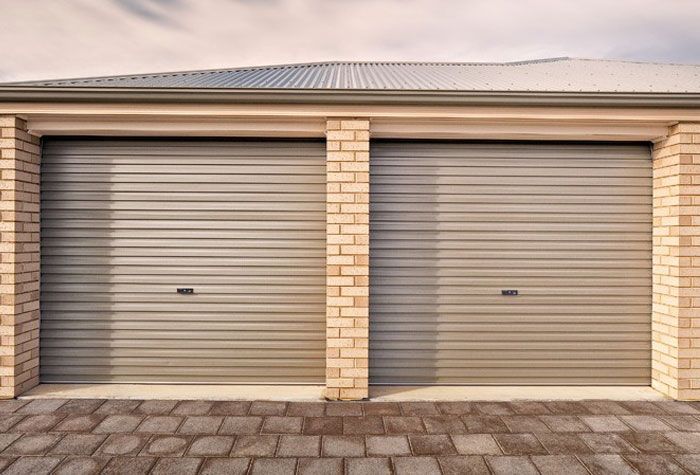 A double garage with two side-by-side brown metal roller doors set in a brick exterior with a paved driveway.