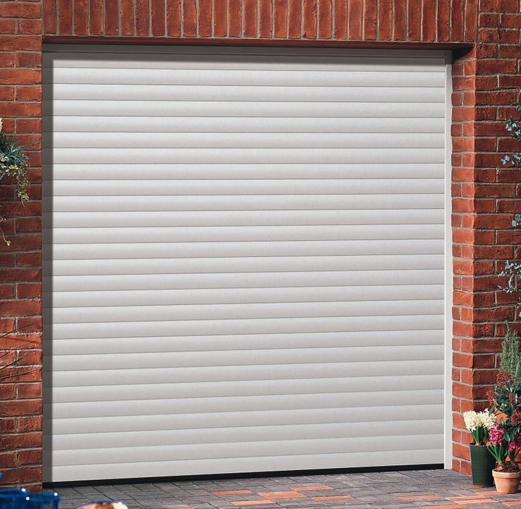 A white, horizontal-slatted roller garage door installed in a red brick exterior wall.