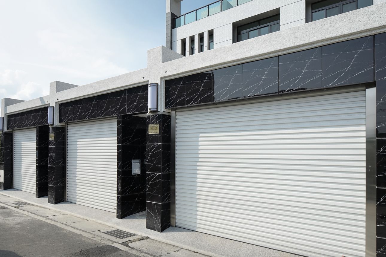 A row of modern townhouses with black marble accents and closed white roller garage doors on a paved street.