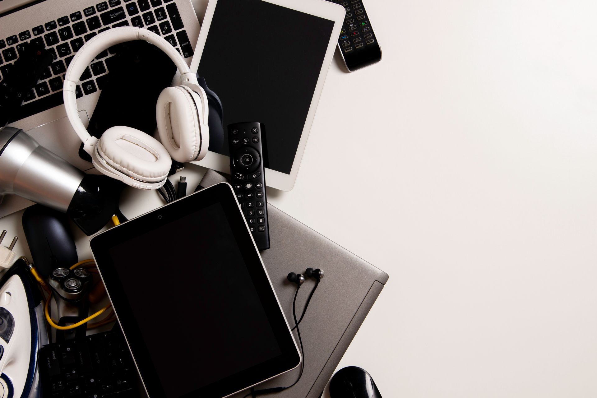 Assortment of electronics on a white surface: headphones, laptops, tablets, remote, and phone.