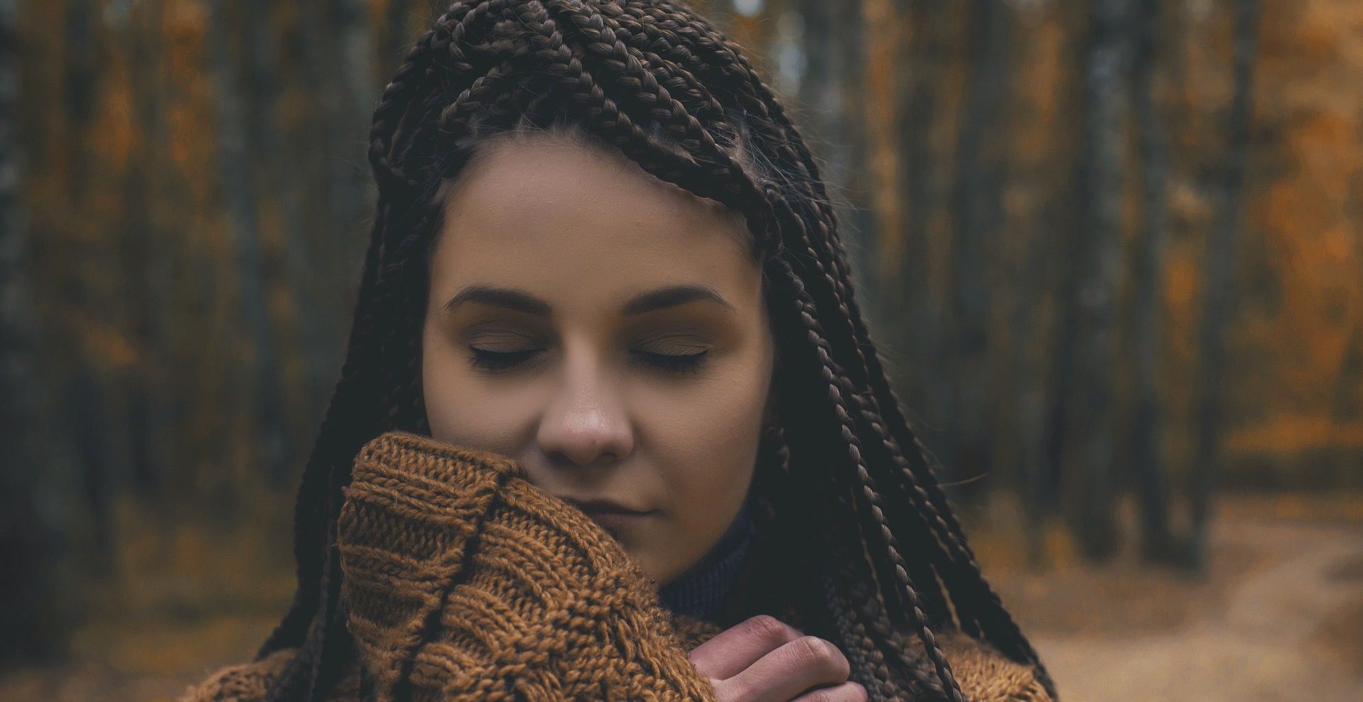 Young woman with long hair and eyes closed stands in a forest and remembers someone fondly