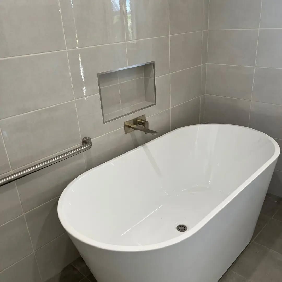 A White Bathtub Is Sitting in A Bathroom Next to A Tiled Wall — Bowral Bathrooms in Exeter, NSW