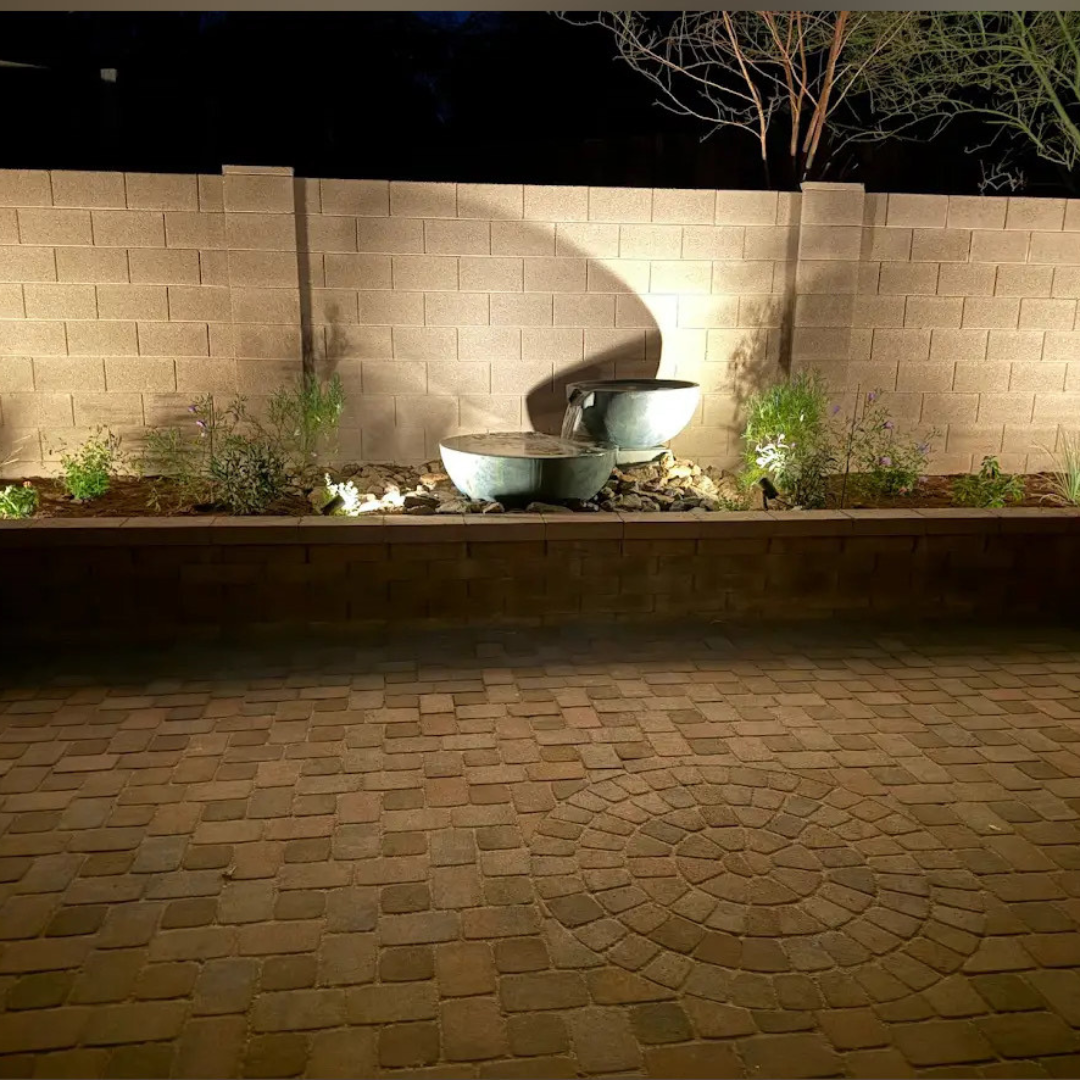 A brick wall with a fountain in the middle of it is lit up at night.