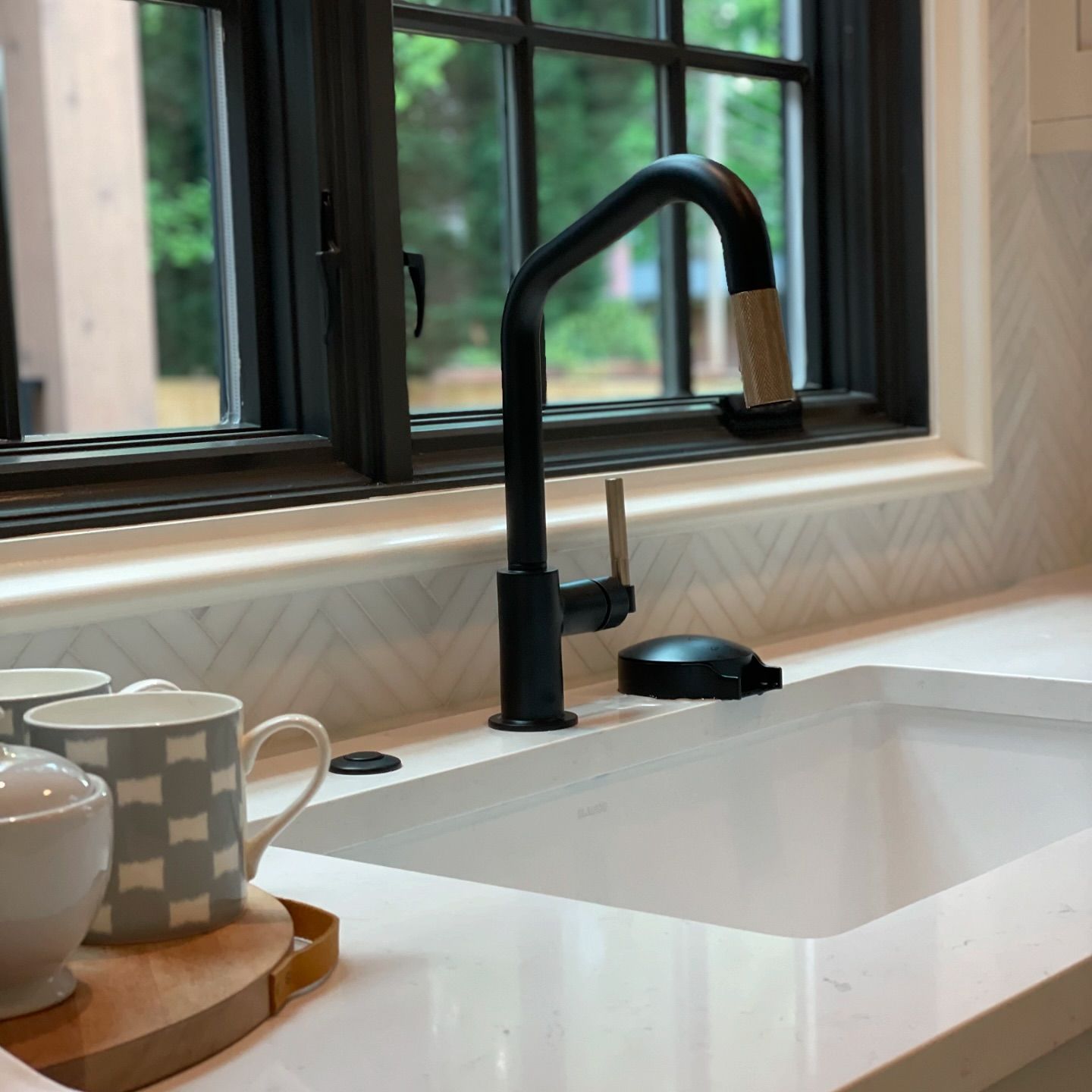 A kitchen sink with a black faucet next to a window