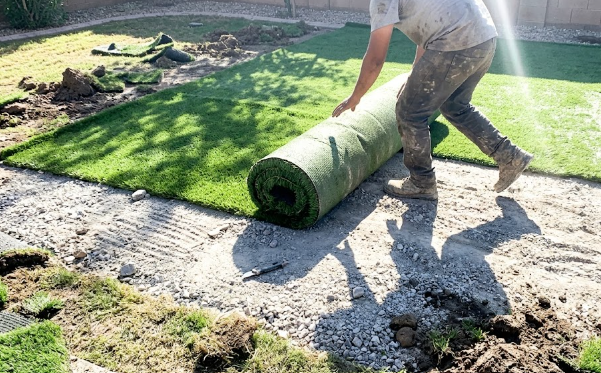 Professional installation team laying down a fresh roll of artificial grass in a backyard.