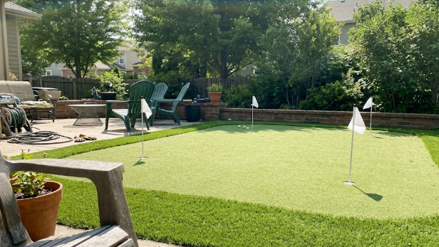 A custom backyard putting green made from artificial turf next to a modern patio.