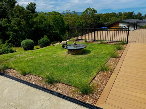 Lush green lawn with fire pit, bordered by plants and wood decking, overlooking a treed landscape — CAW Services in Badagarang, NSW