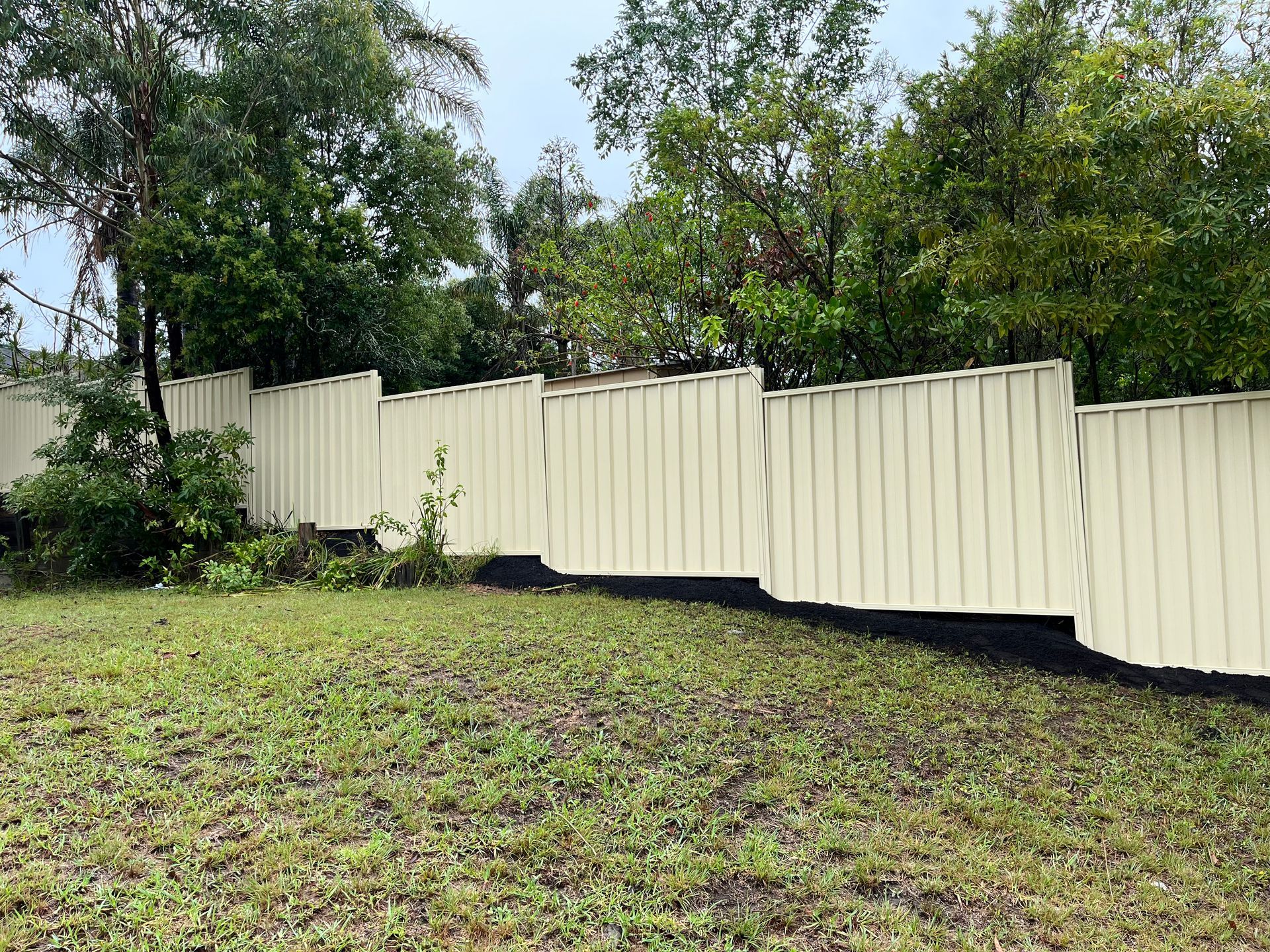 White fence leaning, likely damaged by a storm, in a grassy backyard with trees — CAW Services in Badagarang, NSW