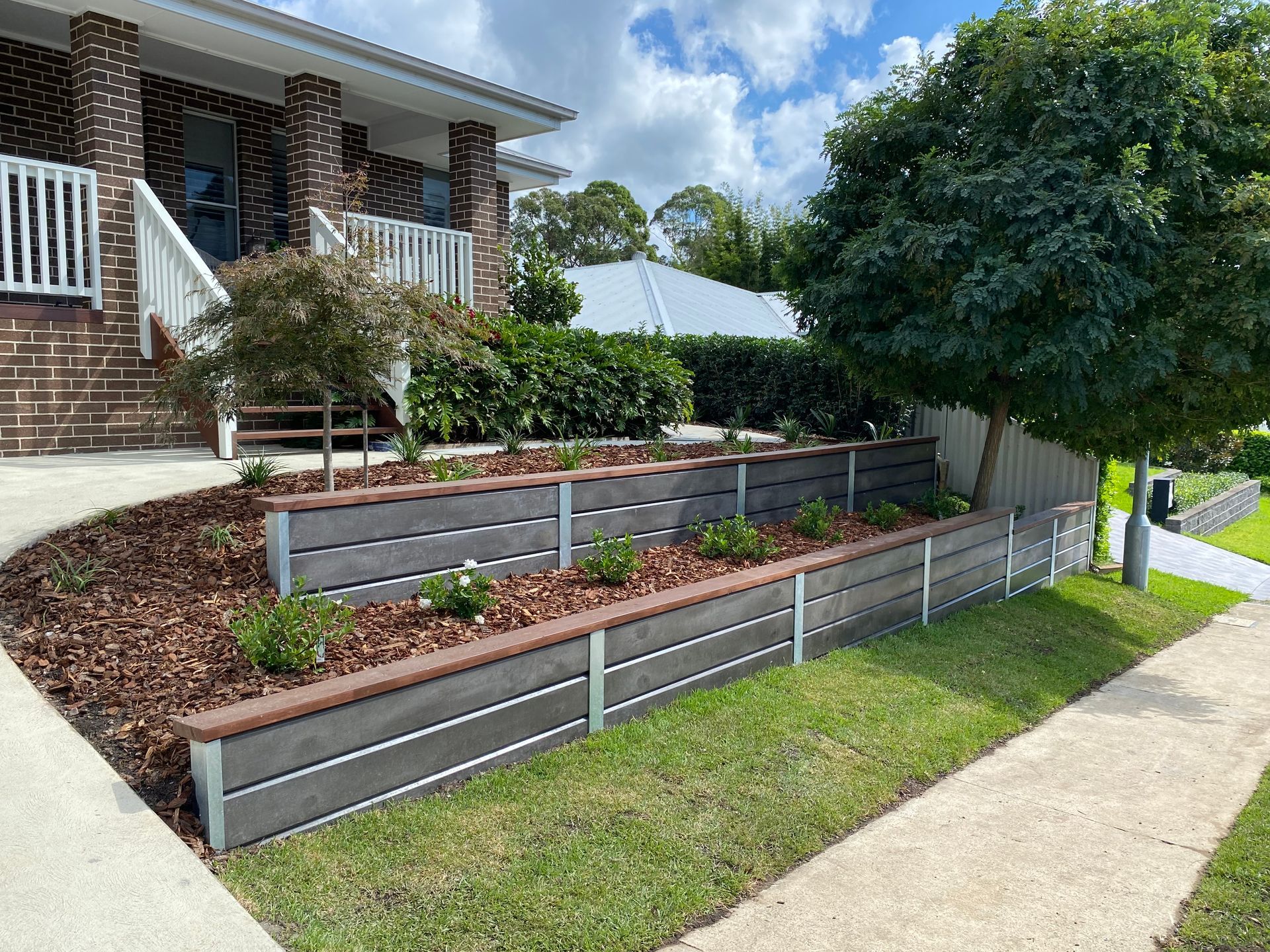 Exterior view of a house with tiered, gray and brown retaining wall planters along a sidewalk. — CAW Services in Badagarang, NSW