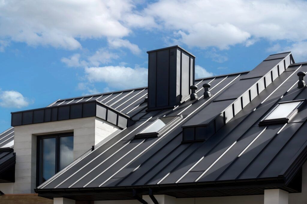 Black Metal Roof With a Chimney, Skylights, and a Bright Blue Sky — CAW Services in Badagarang, NSW