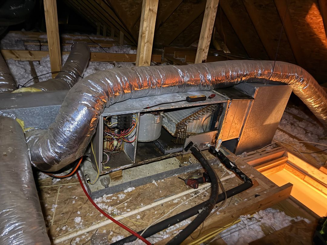 Insulated HVAC duct and furnace unit in a dusty attic with exposed rafters.