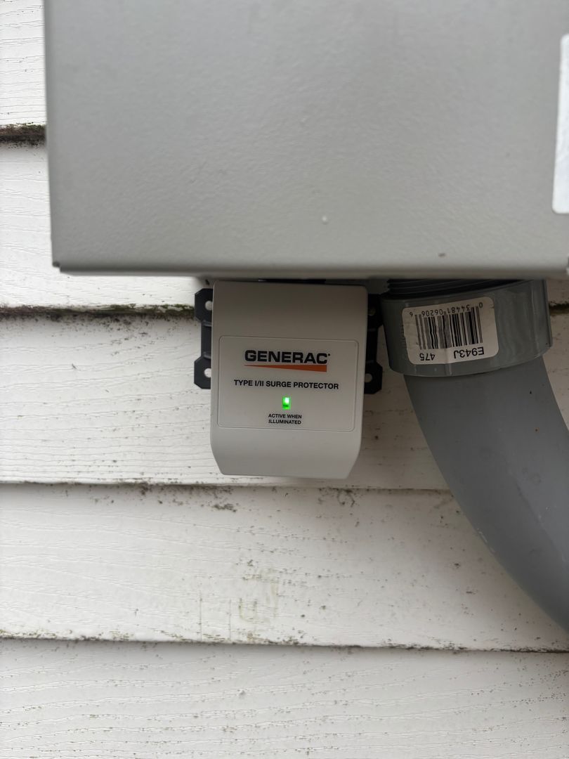 Gray Generac generator transfer switch mounted on white siding with green status light