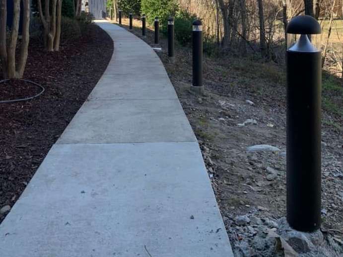 Curved concrete walkway through a wooded area with black light posts along the path