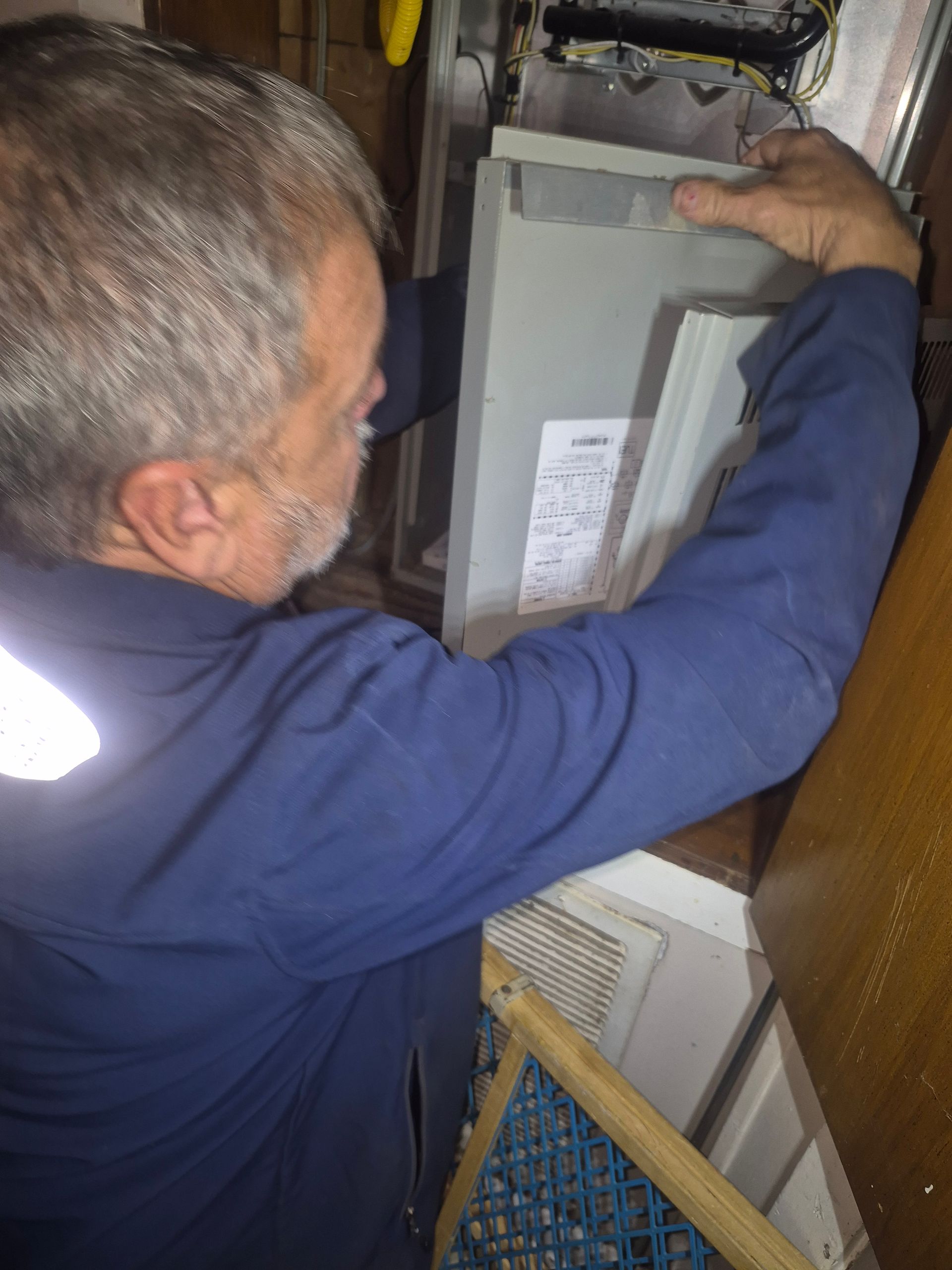 Worker in blue coveralls inspecting an electrical panel with the cabinet open indoors.