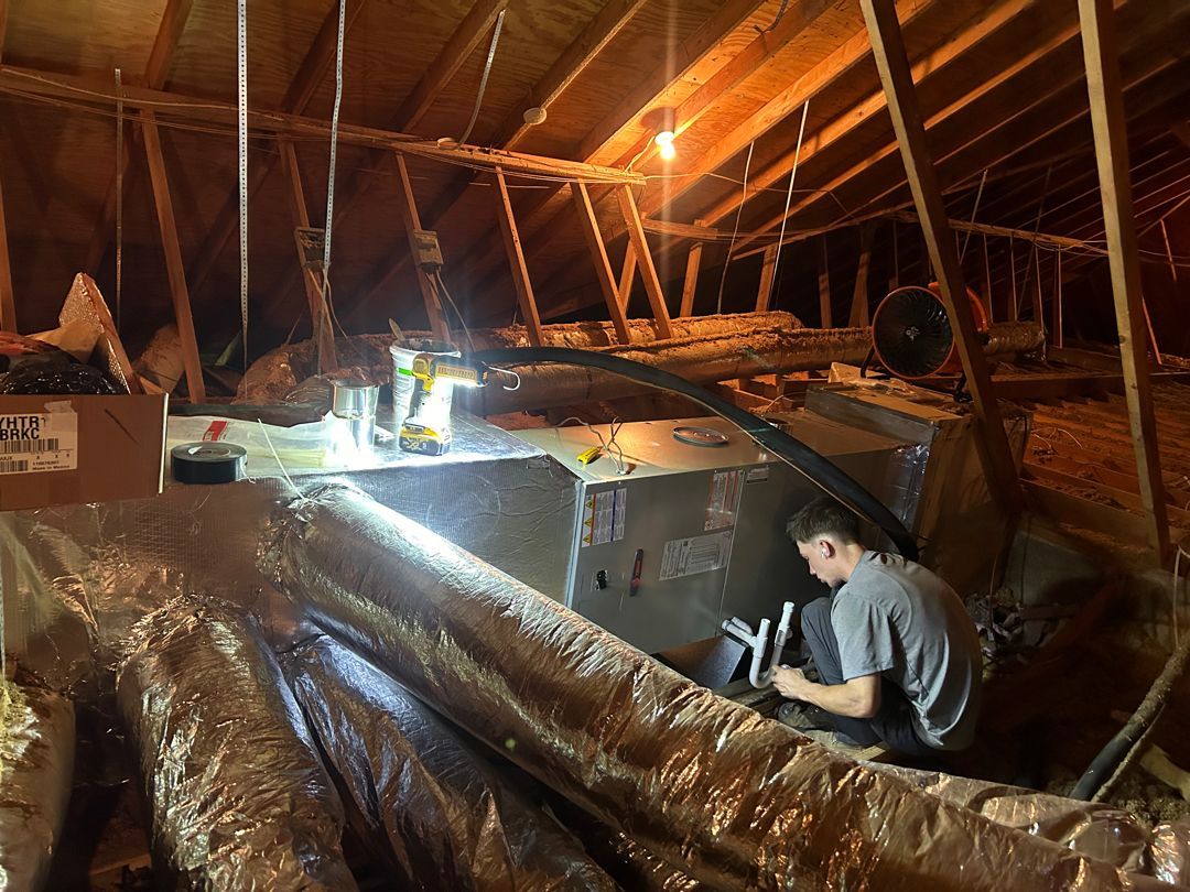 Person working in a dimly lit attic with exposed beams and reflective insulation sheets