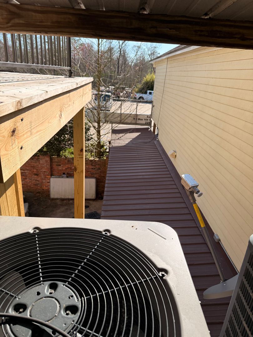 Rooftop HVAC fan in foreground, overlooking a narrow alley beside beige siding and a wooden deck.