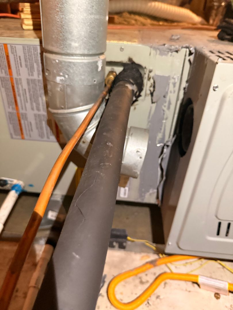 Close-up of furnace ductwork with a black insulated pipe and orange cord beside a white HVAC unit