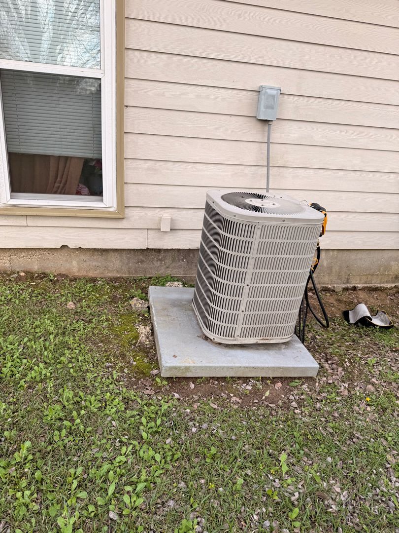 Outdoor air conditioner unit beside house on a concrete pad, with grass and a window nearby