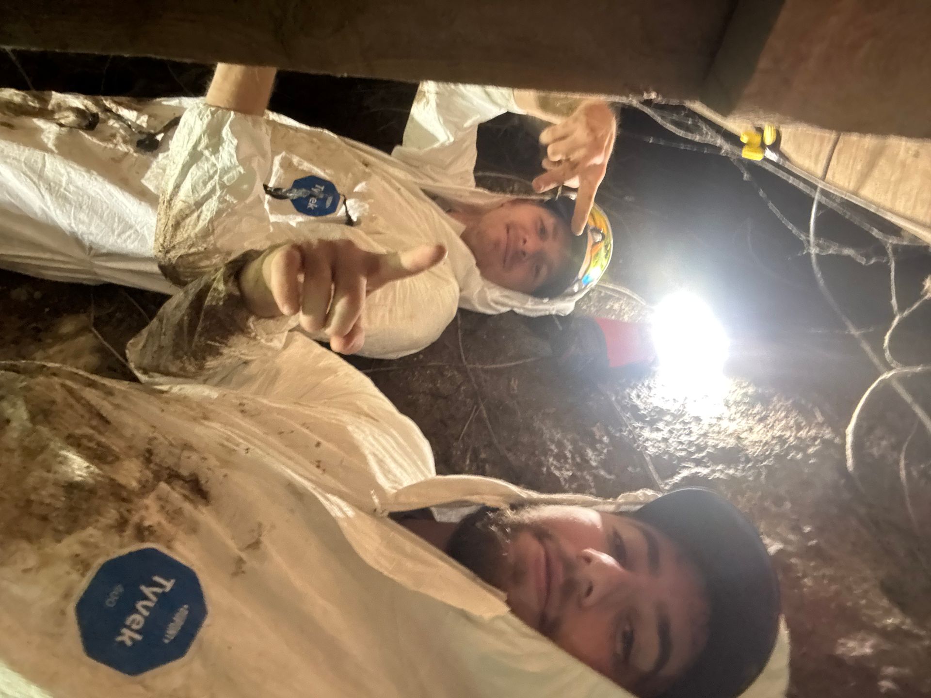 Two people in a tent smiling, one holding a bottle, with a bright light overhead