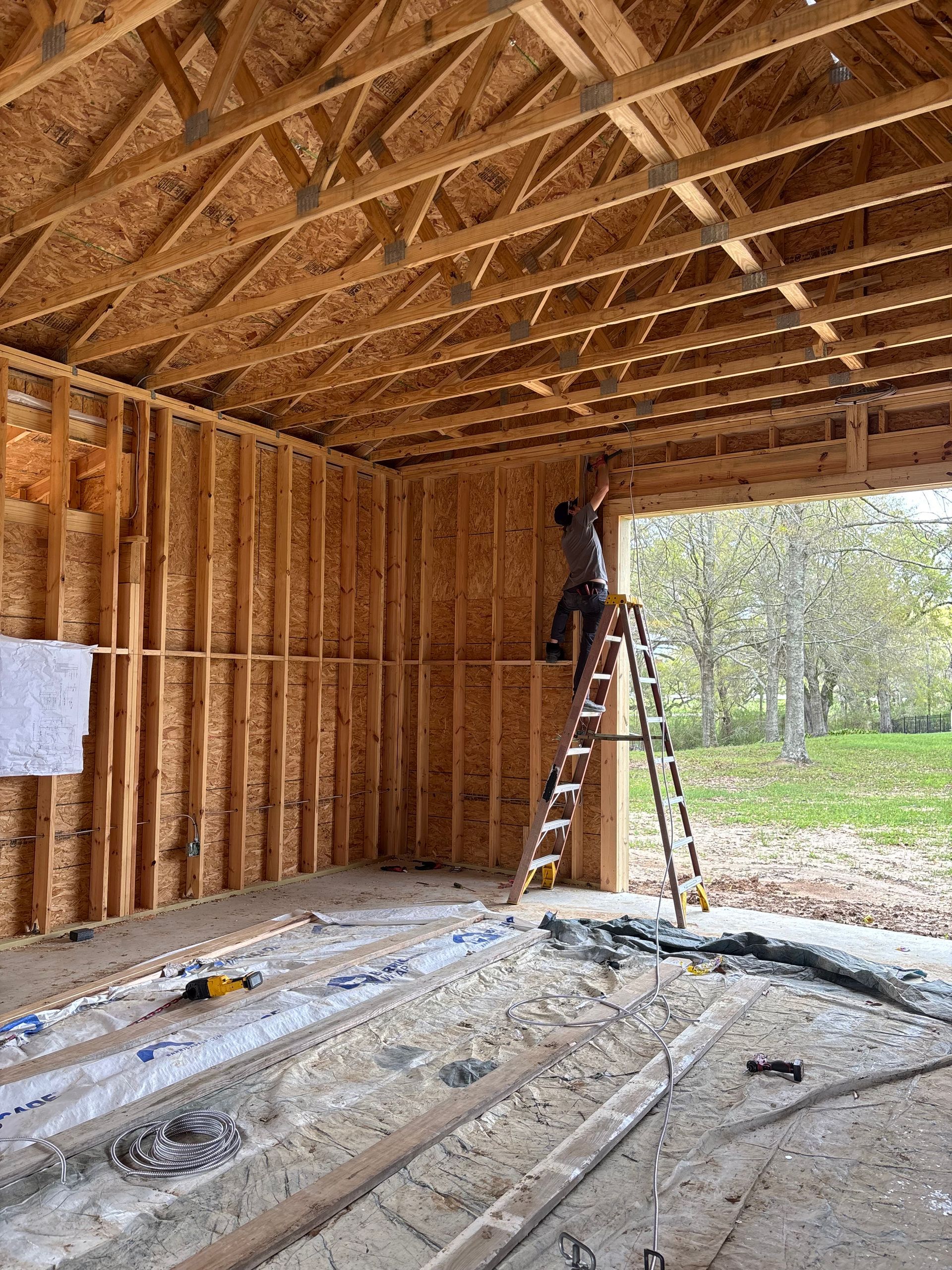 Interior of a wooden house under construction, with two ladders and exposed framing.