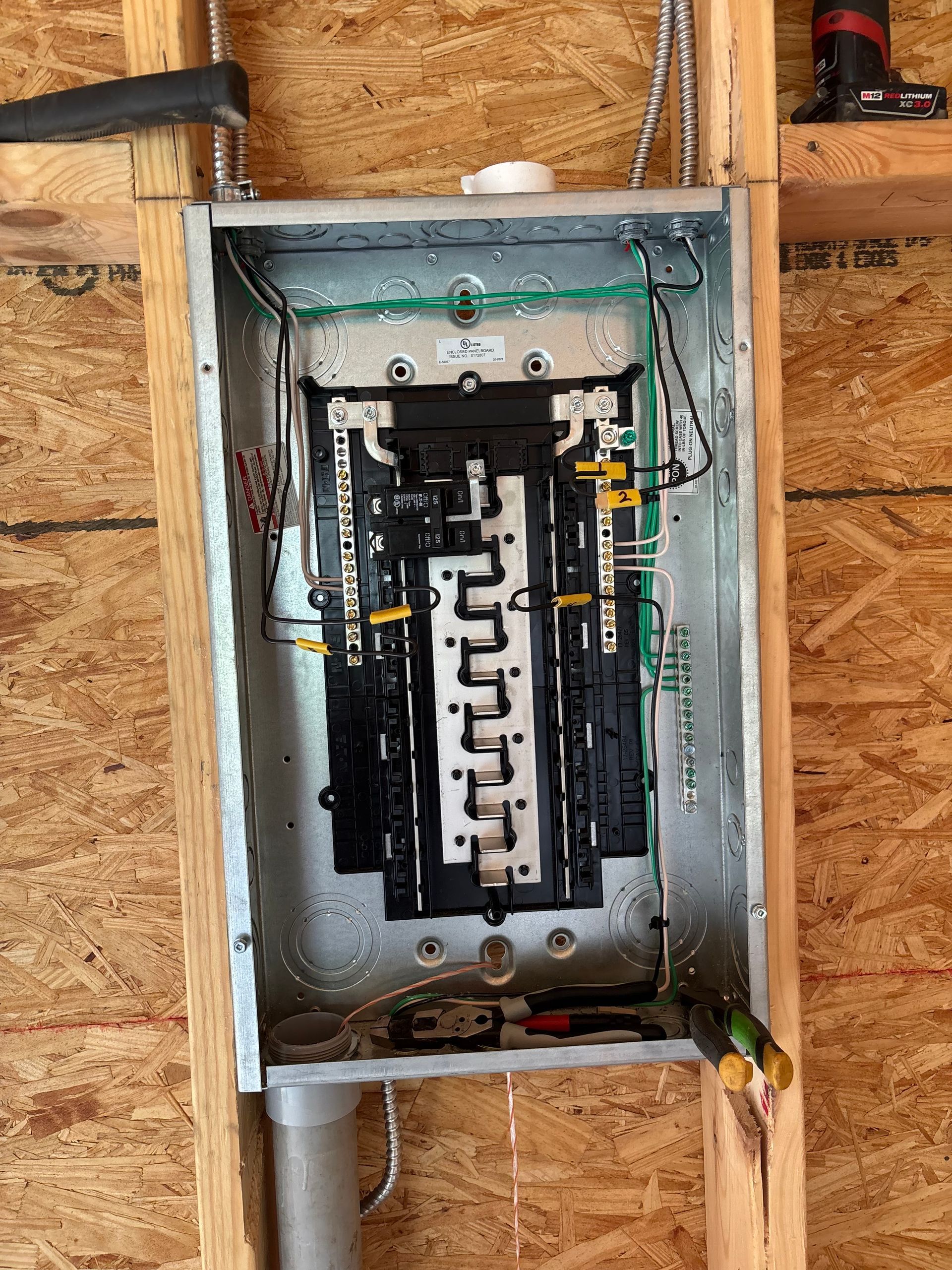 Open electrical breaker panel with exposed wiring mounted in a wall cavity
