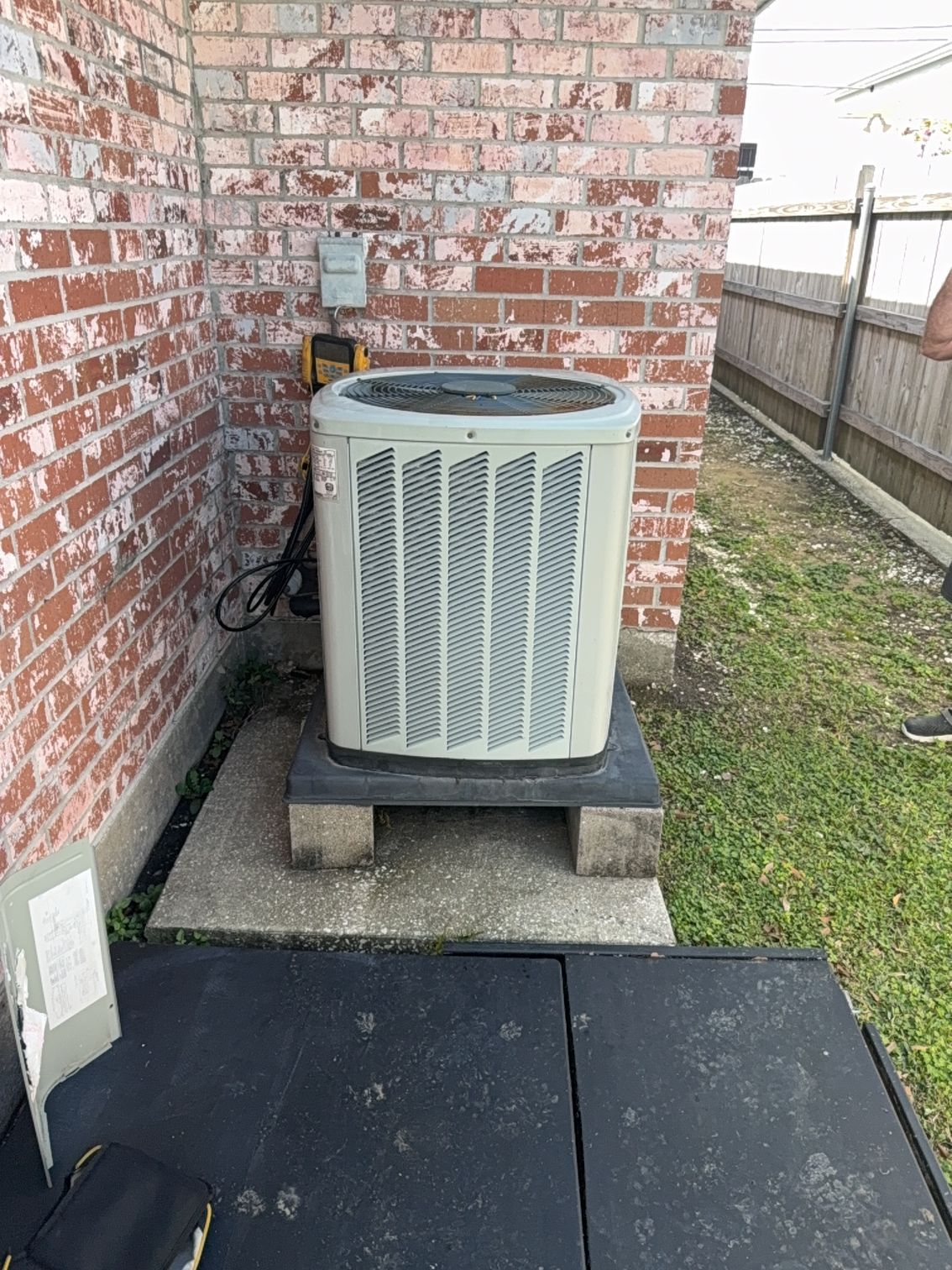 Outdoor air conditioner unit beside a brick house wall on concrete blocks.