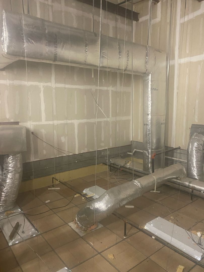 Insulated ductwork and ventilation pipes in an unfinished room with exposed walls and tiled floor
