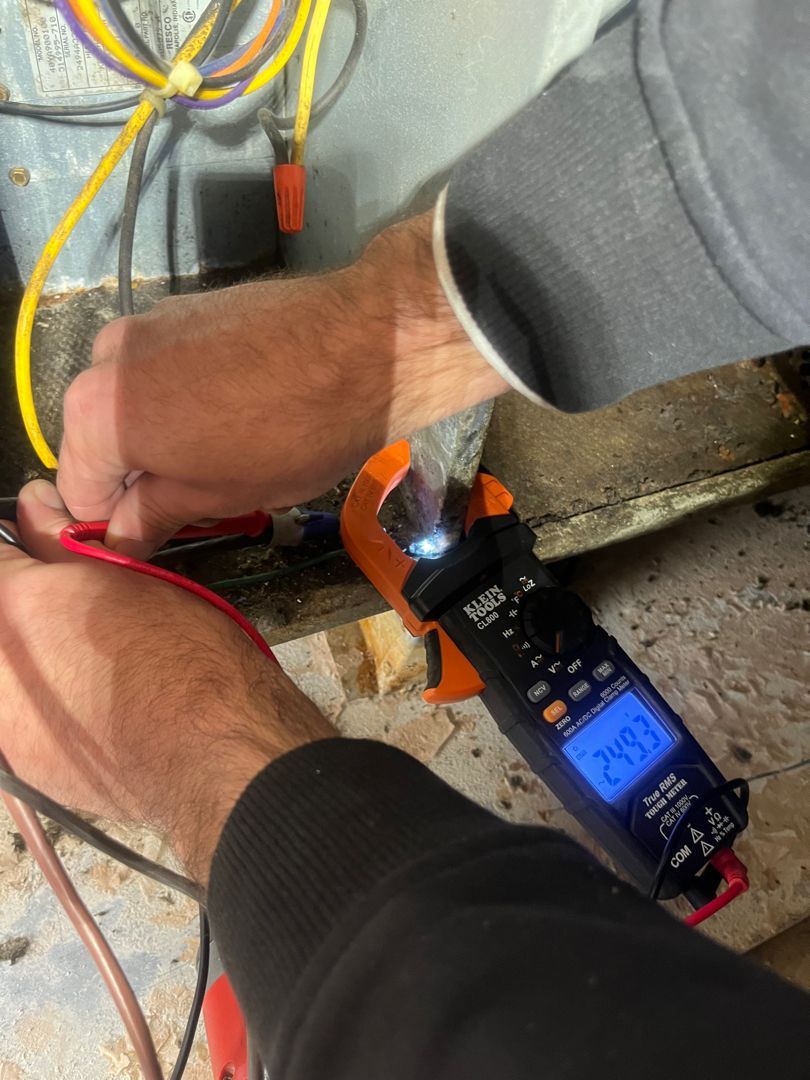 Hands using a meter probe to test wiring on a floor near an outlet and cable junction.