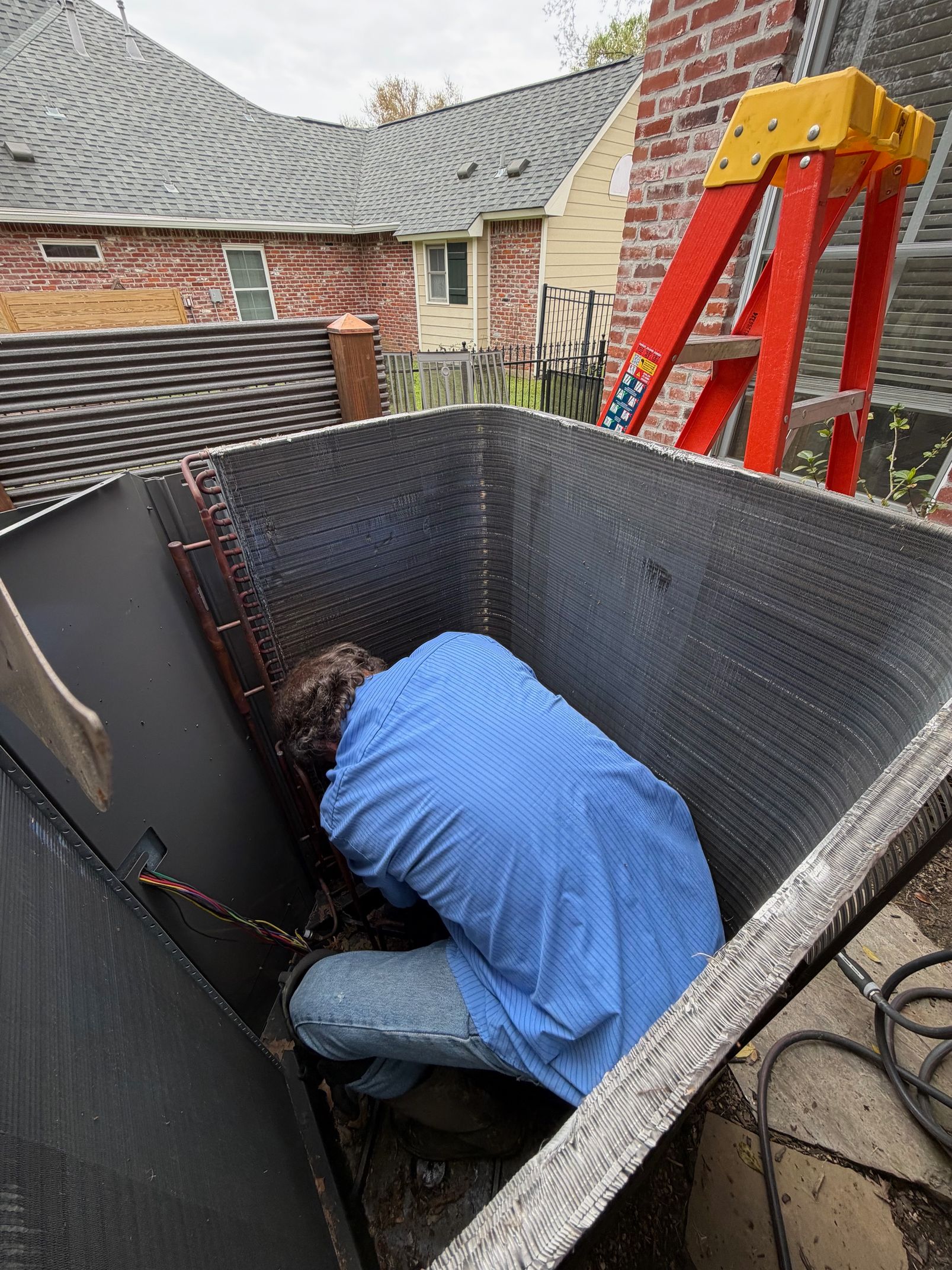 Worker crouching inside a large black bin on a rooftop, with a red ladder nearby.