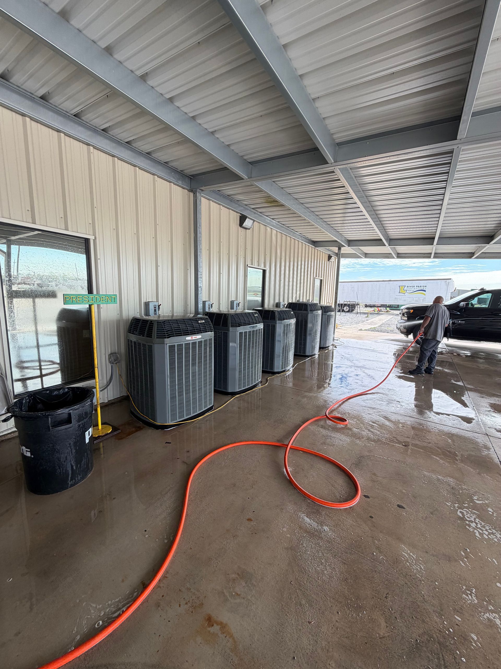 Covered outdoor wash area with trash bins, wet concrete floor, and orange hose by corrugated metal wall