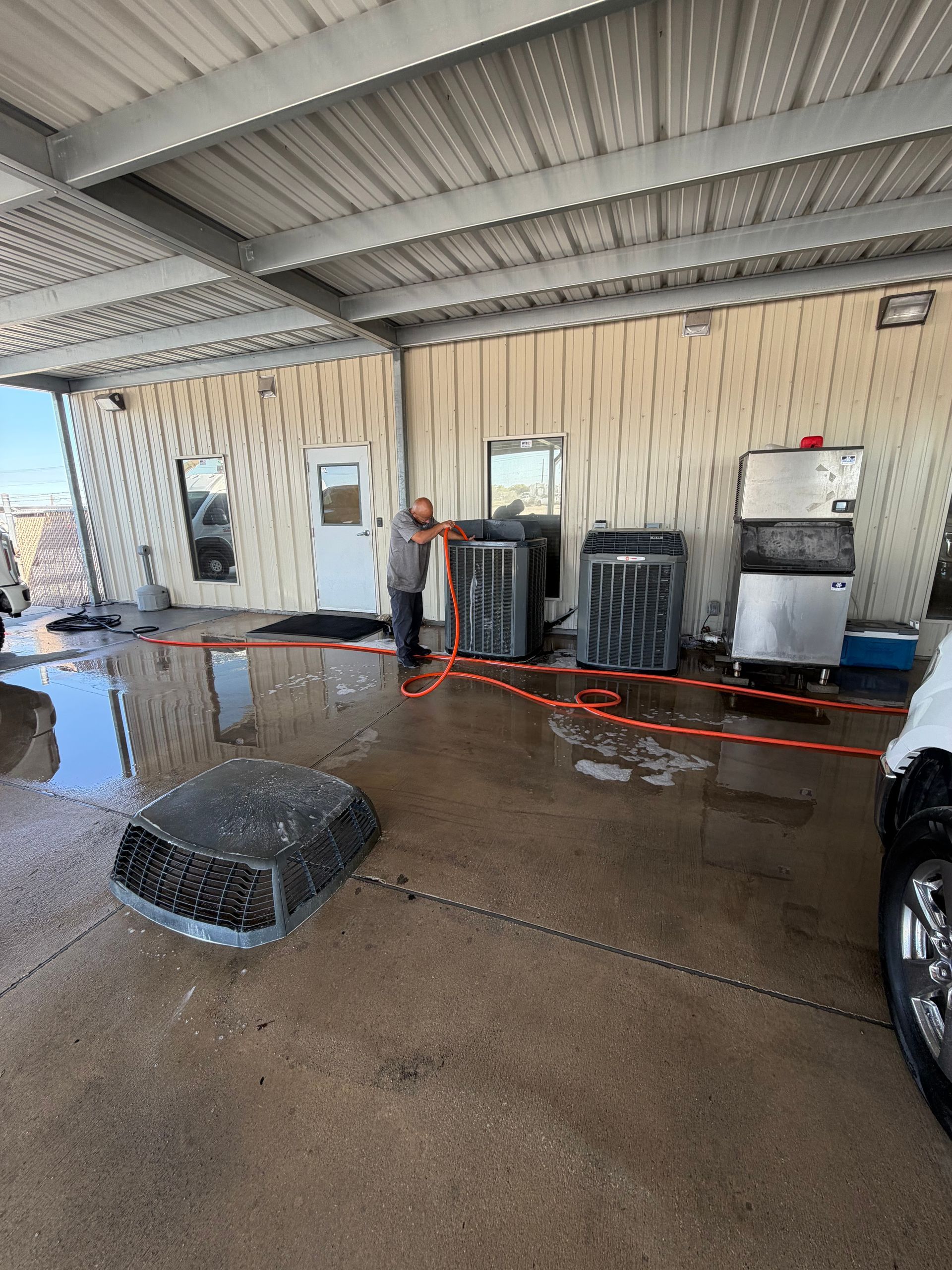 Covered car wash bay with wet concrete, hoses, a drain, and cleaning equipment under a metal roof