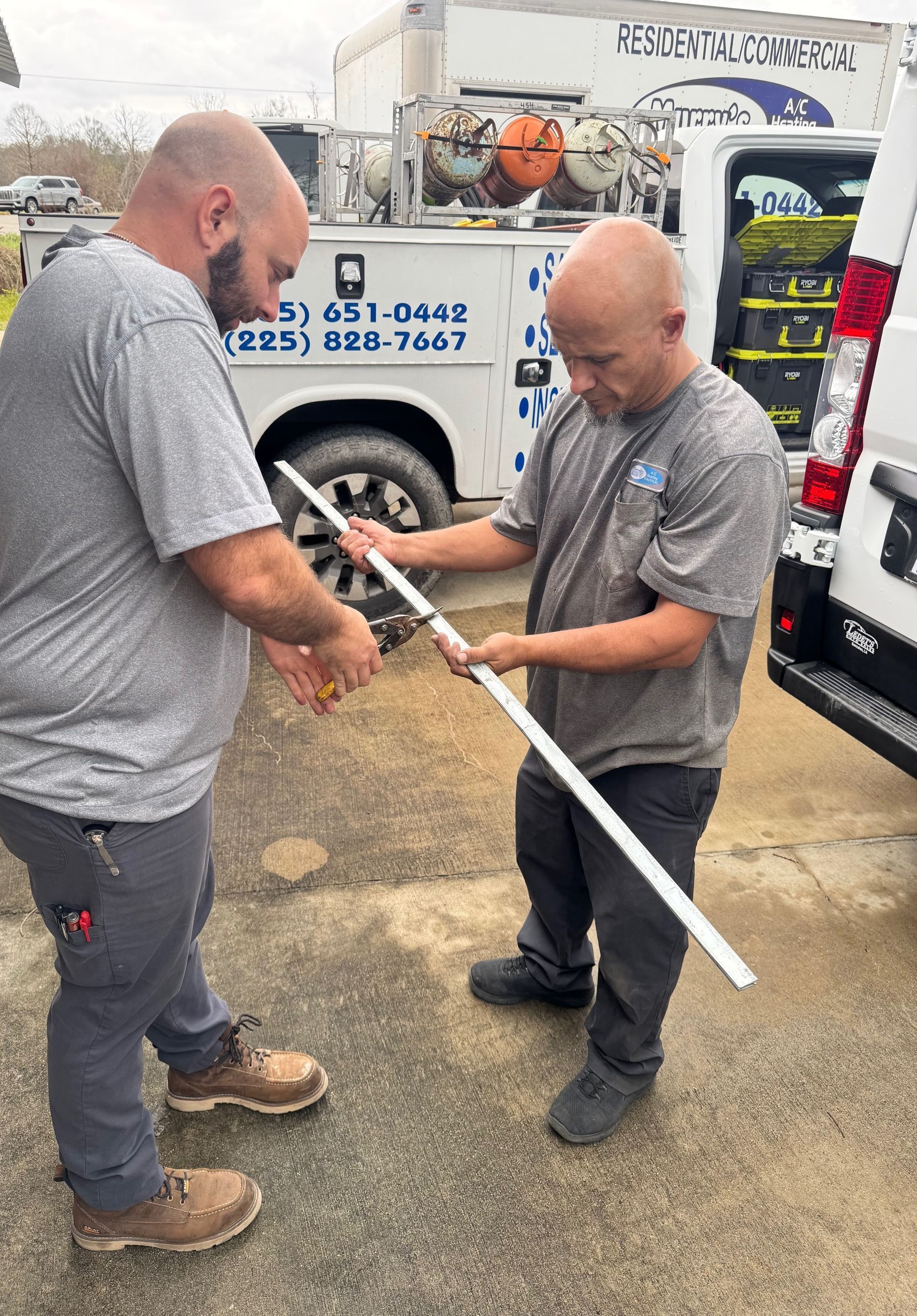 Two men in gray shirts working with a long white pole beside a service truck.