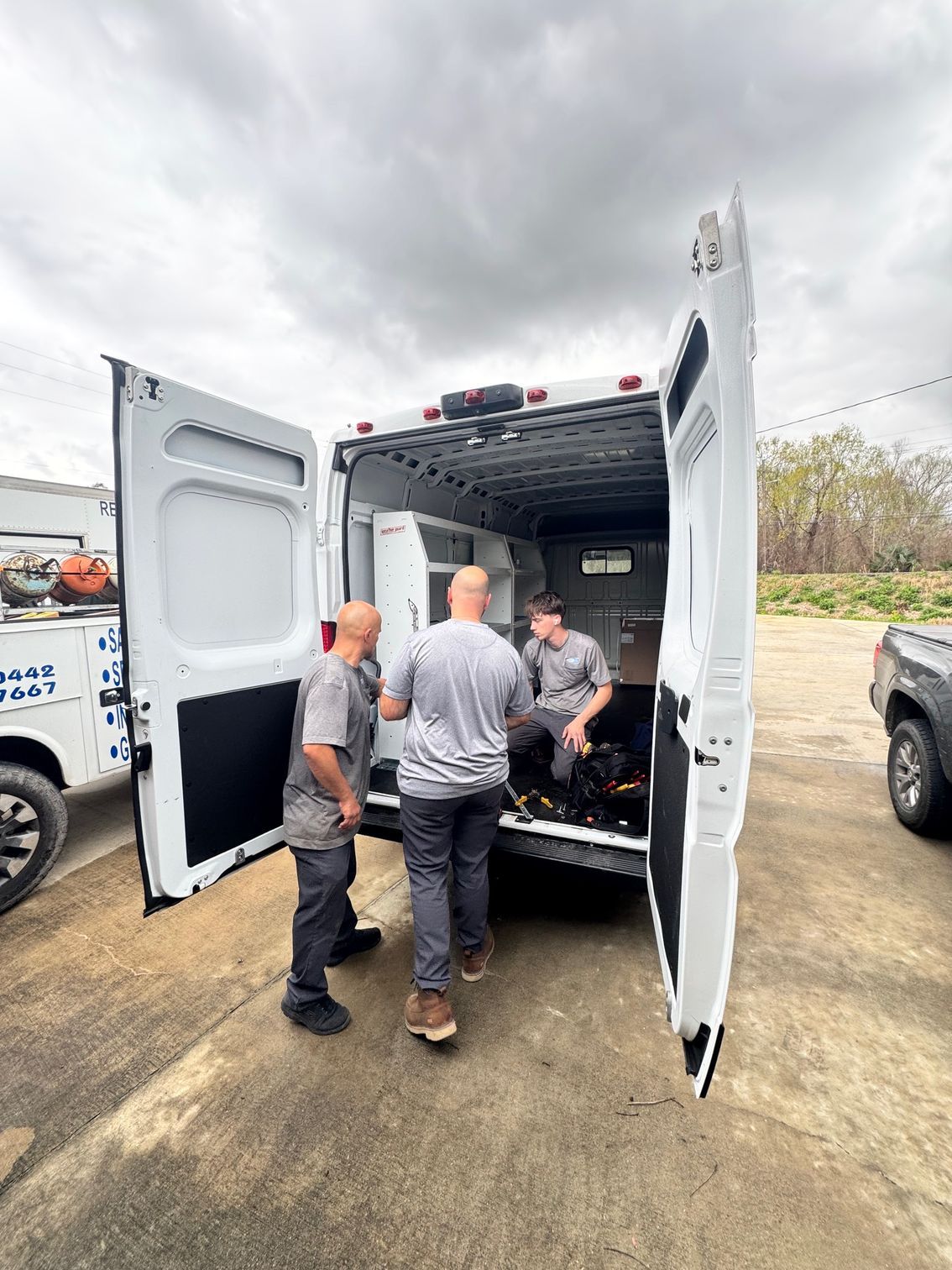 Workers loading equipment into the back of a white utility van outdoors