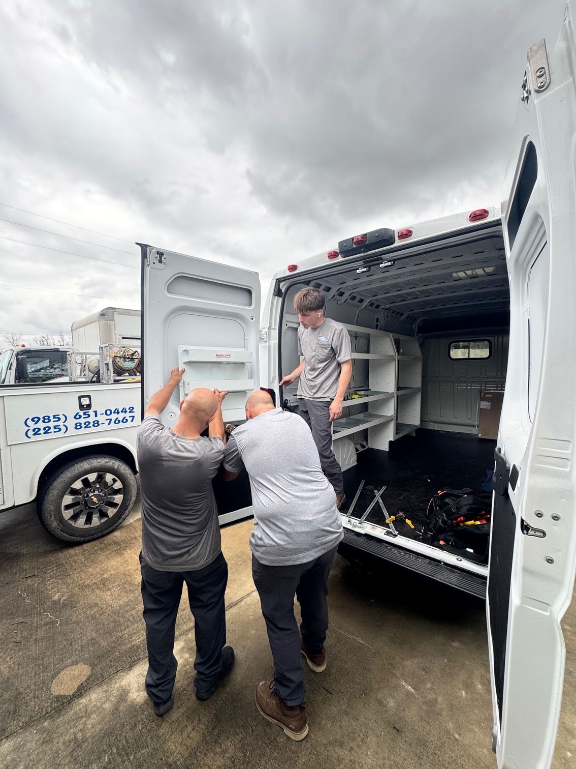 Workers unloading equipment from a white truck in a parking lot under cloudy skies