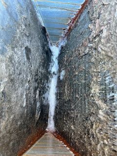 Narrow gap between two rough concrete walls with a white streak of ice or frost in the center